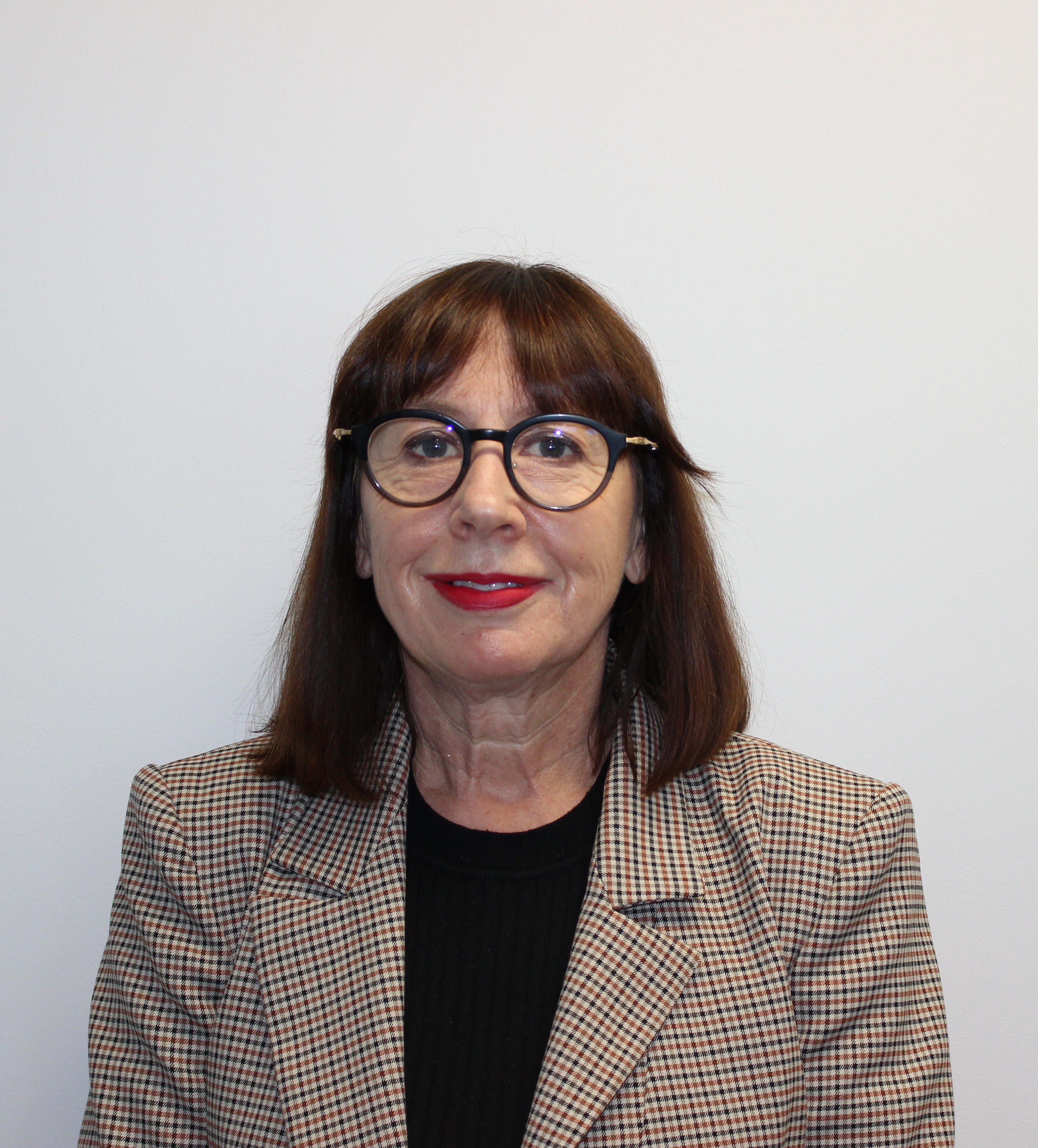 Portrait of a person wearing round glasses, a patterned blazer, and a black top, facing the camera against a plain light background.