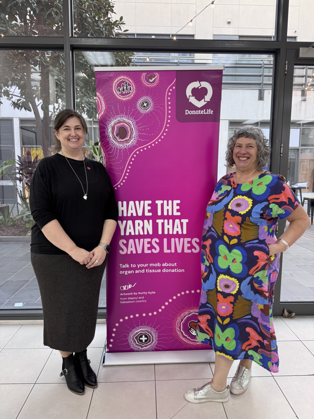 2 people stand beside a DonateLife banner featuring a heart logo and the message: 'HAVE THE YARN THAT SAVES LIVES. Talk to your mob about organ and tissue donation.' 