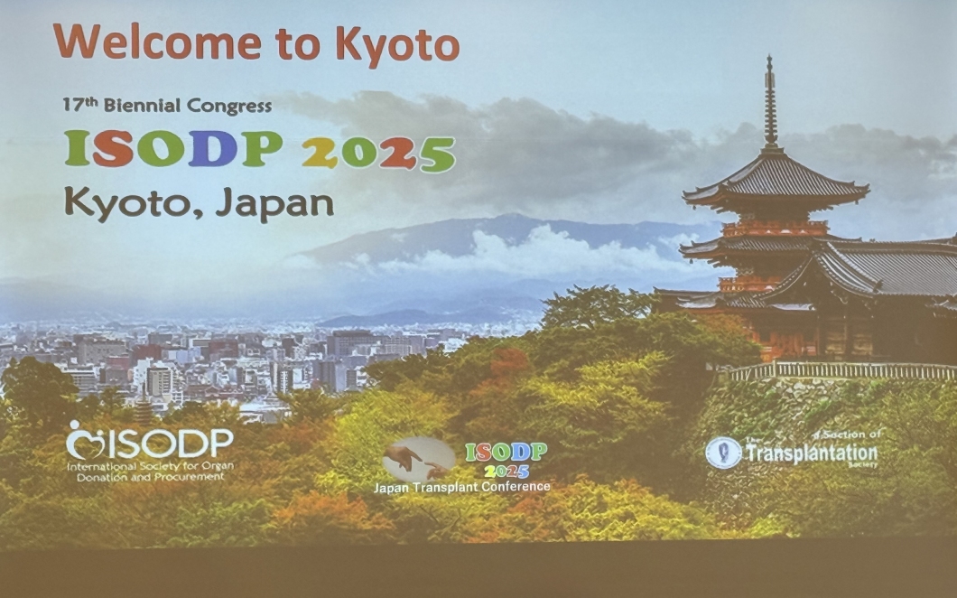 A projection screen displays a welcome slide for the ISODP 2025 conference. The slide features the text ‘Welcome to Kyoto,’ ‘17th Biennial Congress,’ ‘ISODP 2025,’ and ‘Kyoto, Japan’. The background shows a scenic view of Kyoto with a traditional pagoda on the right, lush green trees in the foreground, and the city skyline and mountains in the distance. Logos for ISODP, the Japan Transplant Conference, and the Transplantation Society appear along the bottom of the slide.