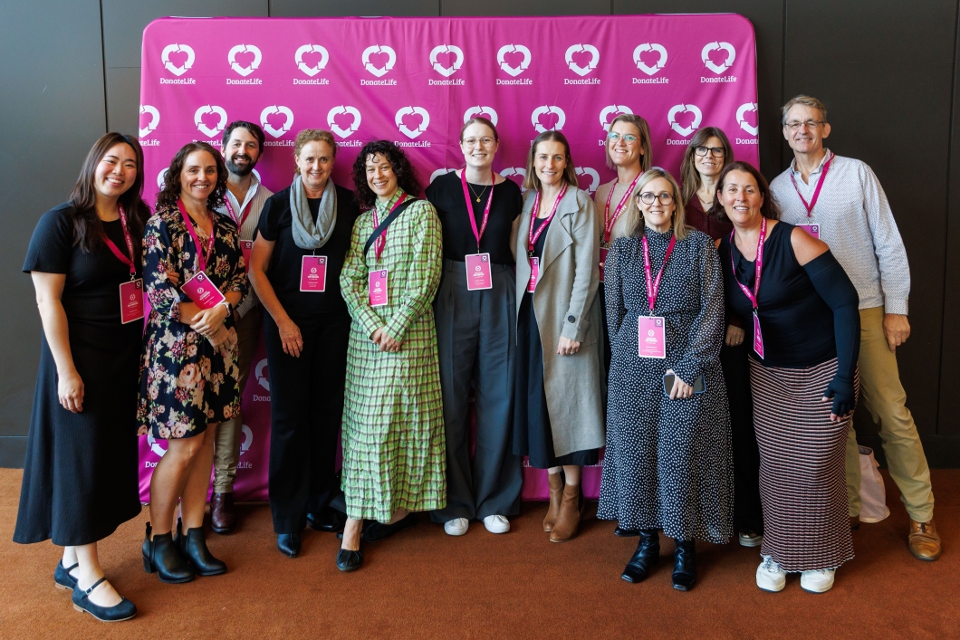 A group of people posing for a group photo in front of a magenta DonateLife banner.