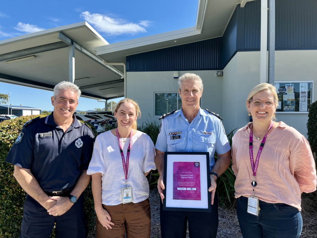 Four individuals stand outside a building, proudly holding a framed recognition award for the Sunshine Coast Highway Patrol.