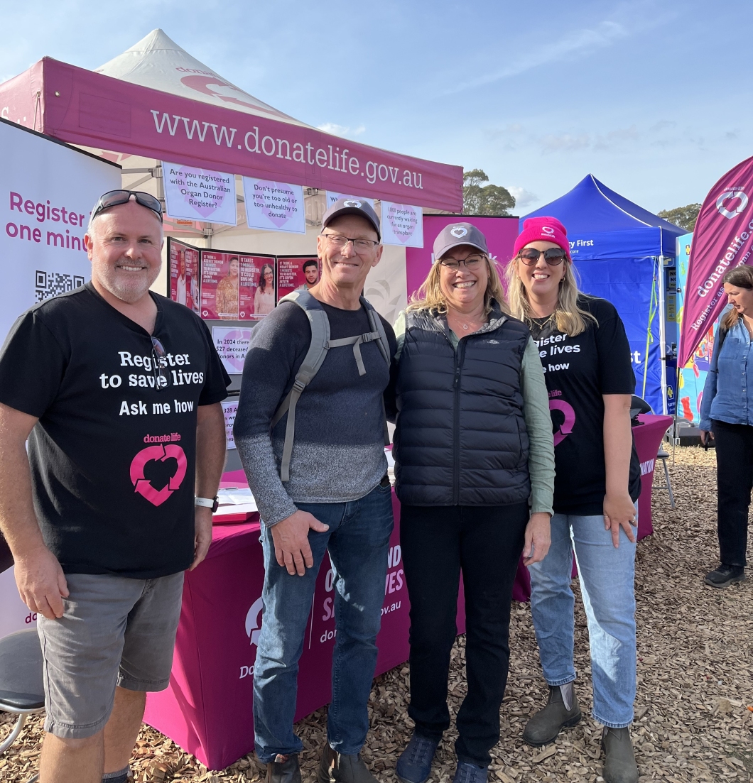 Four people stand in front of a DonateLife marquee, smiling for a photo together. The event they are at is outside and it’s a clear day with blue skies.