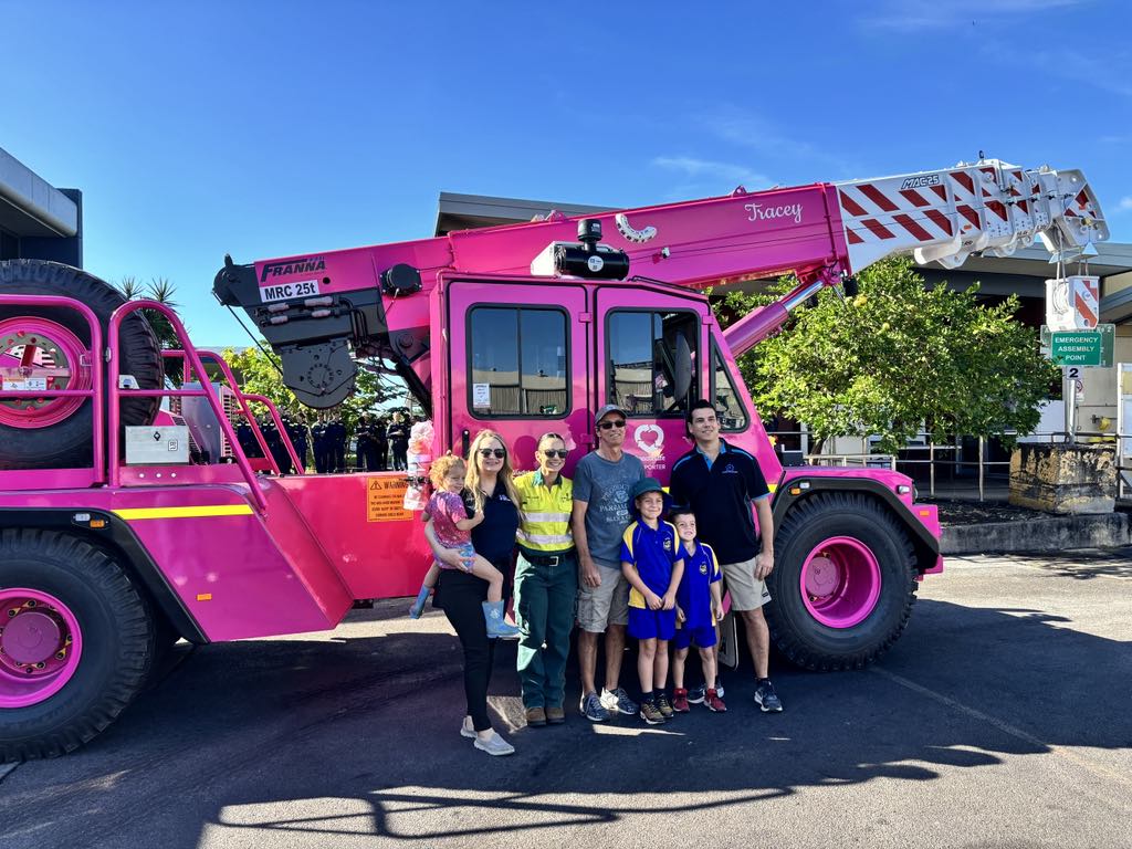 A group of 7 people stand in front of a large pink crane truck labeled 'Tracey' on the arm and 'MRC 25t' on the side.