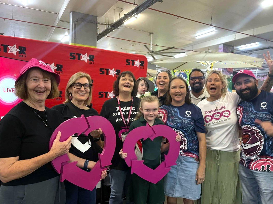 A group of DonateLife volunteers and community members pose in front of a Star FM promotional backdrop, holding large magenta DonateLife symbols during an organ and tissue donation awareness event.