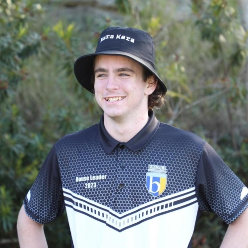 Max standing with hands on hips smiling. He has a black bucket hat on and his school jersey.