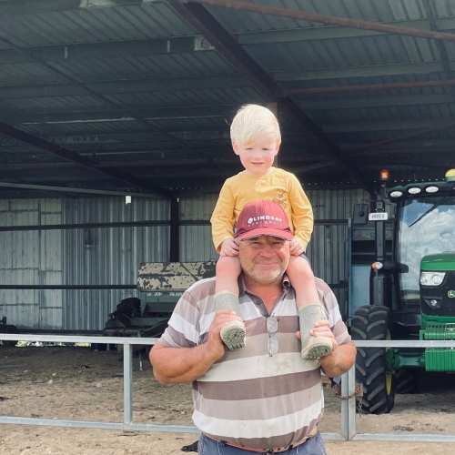 Man in a stripped shirt and jeans, standing with a little boy sitting on his shoulders.