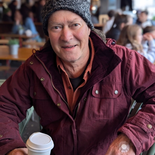 Photo of double lung recipient Paul Sandall wearing a maroon jacket and a grey beanie, holding a white take away coffee cup