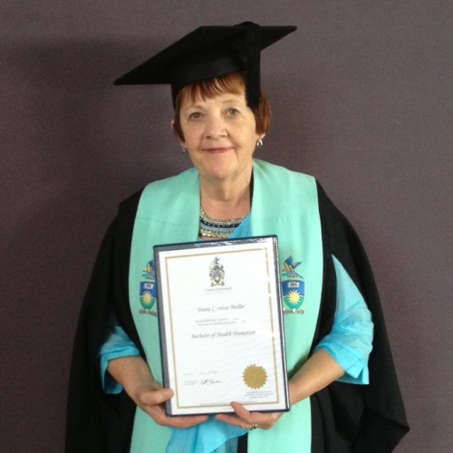 Woman in a graduation gown with teal drapes. She is holding a certificate and is smiling at the camera.