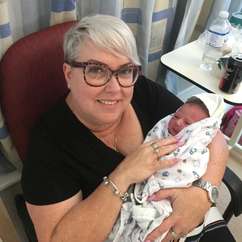 Woman with a short grey bob sitting in a hospital chair, holding a newborn baby