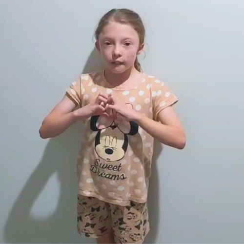 Young girl in a peach coloured polka dot shirt with Mini Mouse in the centre. She is holding her hands in the shape of a heart.