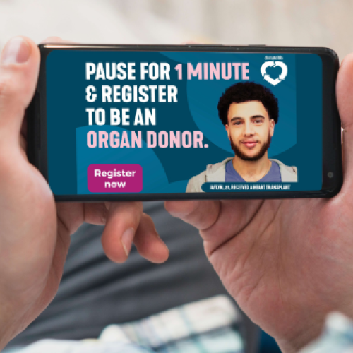 A photo of someone’s hands holding a mobile phone. The phone screen displays an ad for DonateLife, that says ‘Pause for 1 minute and register to be an organ donor’