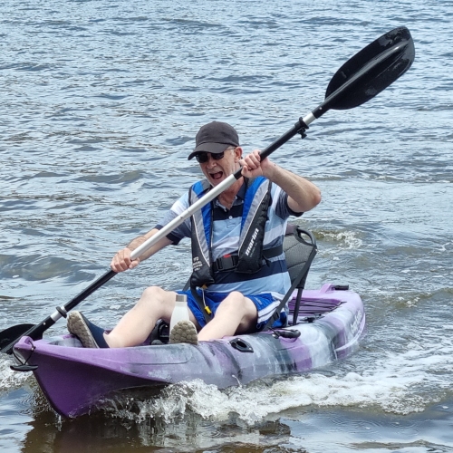 Man in a purple kayak, rowing through water.