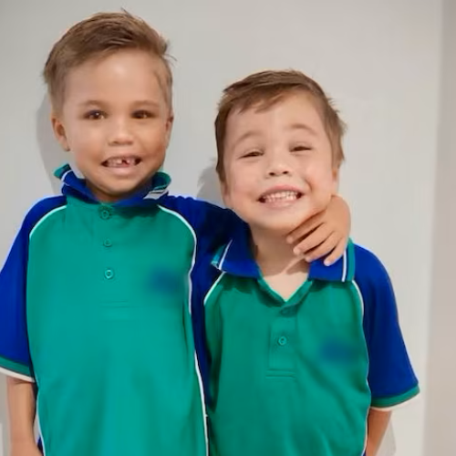 Two young boys in green and blue shirts hugging, smiling at the camera.