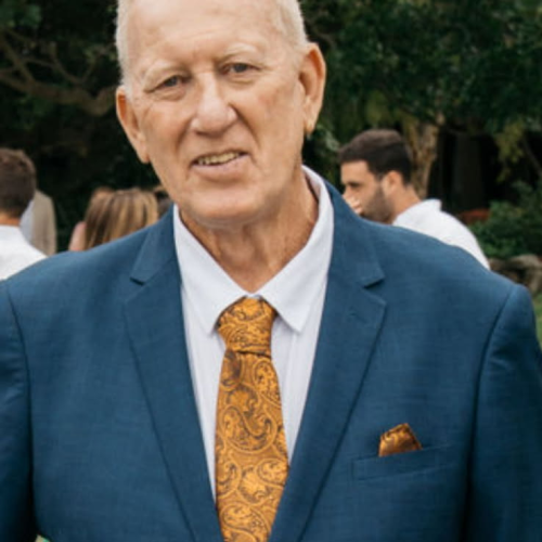 Older man in a blue suit jacket with a yellow patterned tie. 