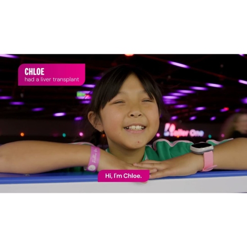 Video still of a child leaning on a barrier in a colourful, neon-lit indoor setting, wearing a wristband and smartwatch; on-screen text reads “Chloe had a liver transplant” and “Hi, I’m Chloe.”