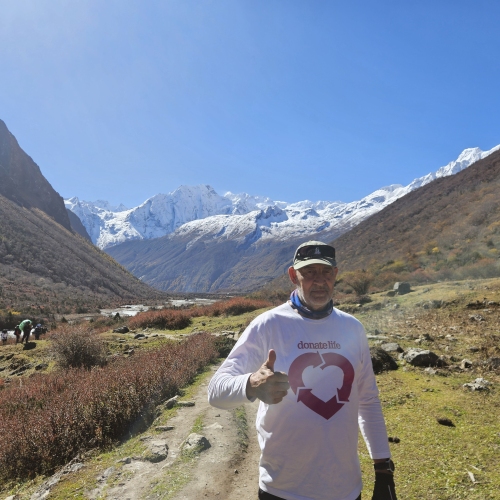 a liver transplant recipient standing outdoors in Nepal with a mountainous landscape in the background.